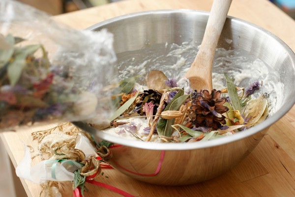 A bag of potpourri being dumped into dough in a metal mixing bowl with a wooden spoon