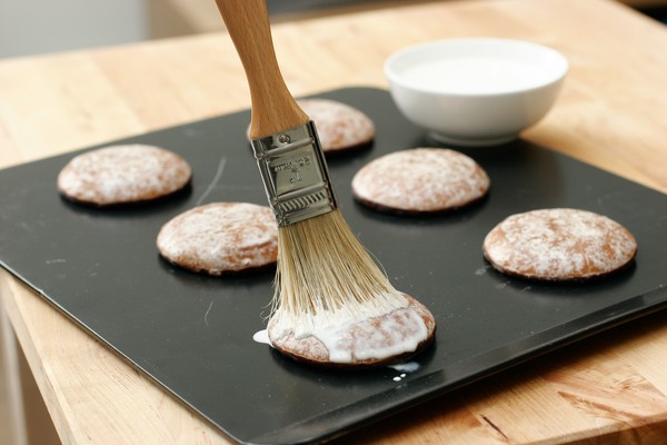 Glazing cookies A pastry brush applying a white glaze to six cookies on a baking sheet; the bowl of glaze is in the background; the cookies now look perfect and have no obvious potpourri sticking out