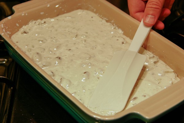 A human hand using a spatula to spread nougat in a rectangular baking dish