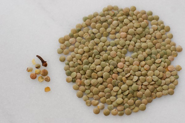 Unsorted lentils spread over a cutting board with broken lentils and a clove sitting next to them