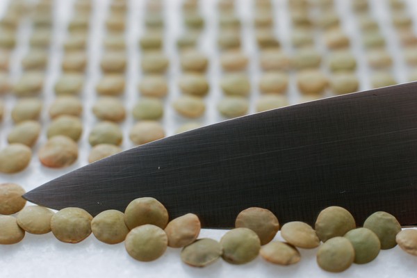 A chef's knife sliding a row of lentils away from neat rows of sorted lentils