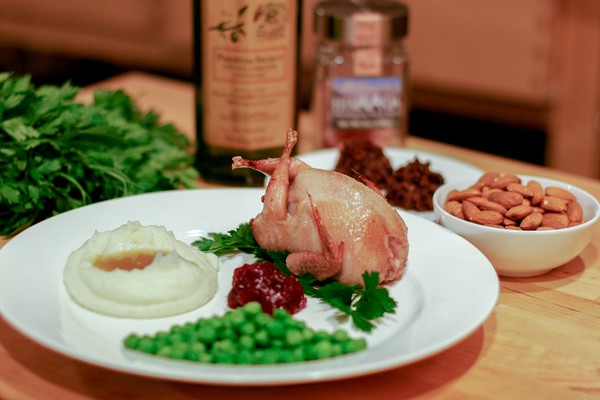 Personal turkey dinner A small cooked bird on a plate along with mashed potatoes and gravy, cranberry sauce, and peas; parsley, a jar of olive oil, a jar of salt, a plate of cookies, and a small white bowl of almonds are in the background