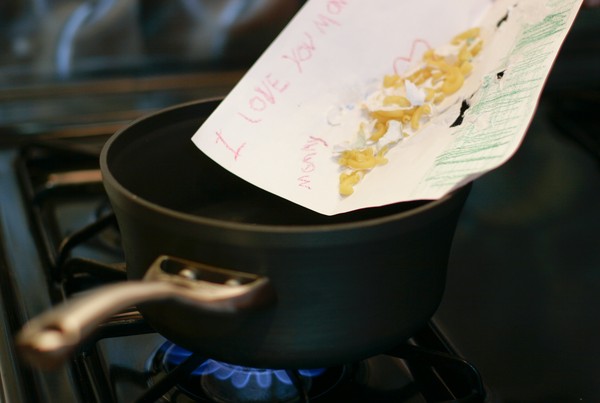 Macaroni being slid off of a macaroni art drawing into a pot of water over a lit burner