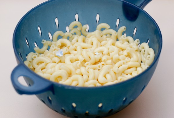 Cooked macaroni in a blue colander; bits of paper remain in the macaroni