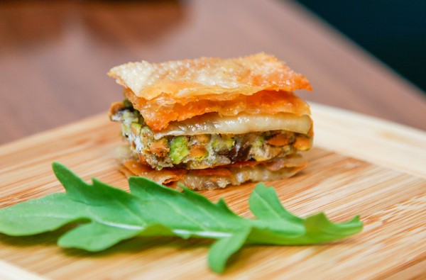 A piece of savoury baklava on a wooden cutting board with a piece of arugula in the foreground