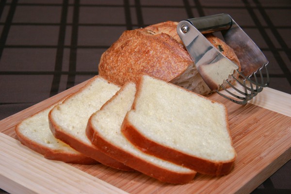 Sliced bread A pastry blender resting on a half of a loaf of sourdough bread with four perfect slices of white bread in the foreground