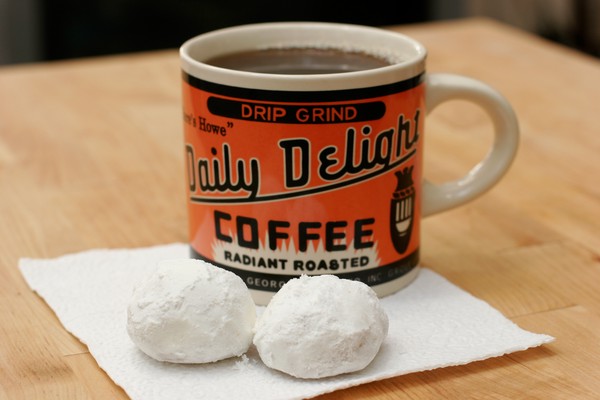 Two biscuits and a cup of black coffee on a white napkin; the coffee mug says, 'drip grind, Daily Delight Coffee, radiant roasted' in black lettering on a bright orange background