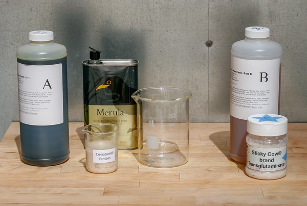 Bottle of unknown substance labeled, 'A'; tin of olive oil; beaker labeled, 'denatured protein'; large empty beaker; bottle of unknown substance labeled, 'B', jar of 'Sticky Cow brand' transglutaminase